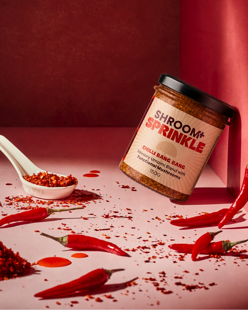 Jar of Acacia Blends 'Shroom+ Sprinkle' with red chili peppers and a spoonful of chilli flakes.